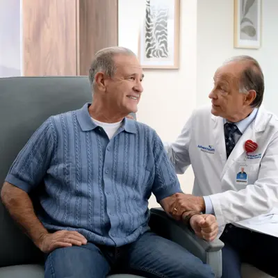 A smiling patient and doctor in a medical office, holding hands and discussing health.
