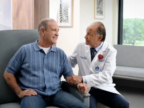 A smiling patient and doctor in a medical office, holding hands and discussing health.