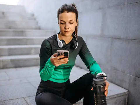 A young female runner takes a break and checks her phone.