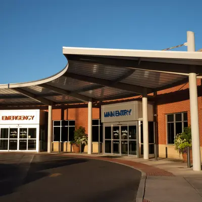 Main entrance of a hospital with emergency and main entry signs, under a curved canopy.