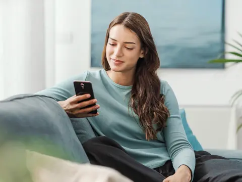 A woman sitting on her couch looking at her phone.