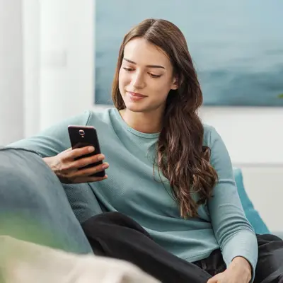 A woman sitting on her couch looking at her phone.