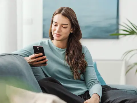 A woman sitting on her couch looking at her phone.