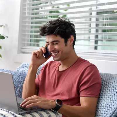 Man sitting on a couch, using a laptop and talking on the phone.