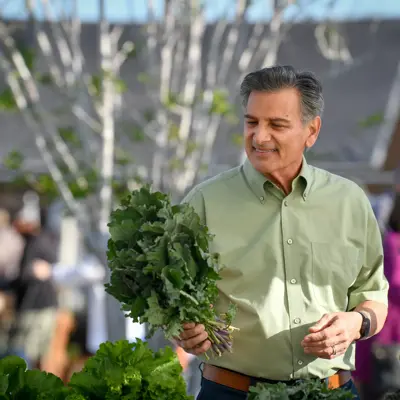 A man in a green shirt holds a bunch of green vegetables at a market.