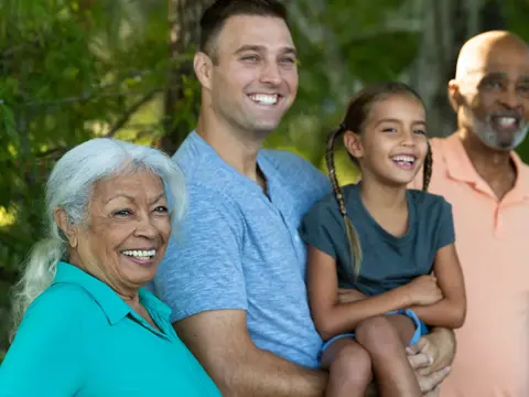 A smiling family of four stands together in a park, showcasing unity and joy.