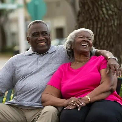 Elderly couple sitting on a bench, smiling and embracing each other in a park.