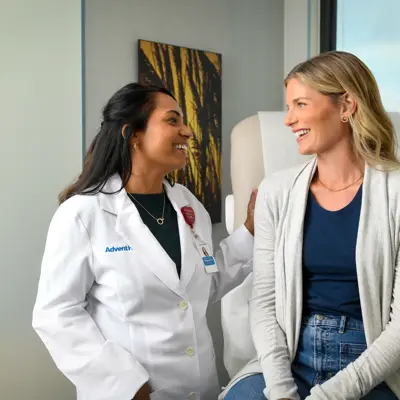 A smiling doctor in a white coat talks to a smiling patient in a medical office.