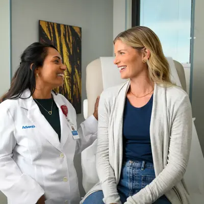 A smiling doctor in a white coat talks to a smiling patient in a medical office.
