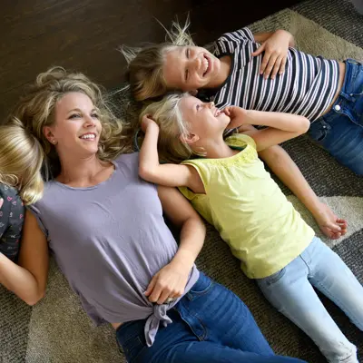 A mother and her three children are lying on the floor, smiling and enjoying each other's company.