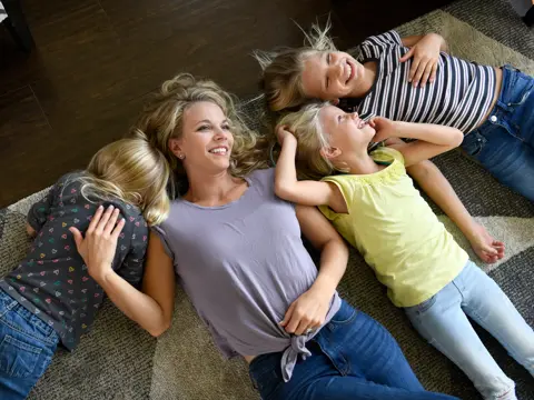 A mother and her three children are lying on the floor, smiling and enjoying each other's company.