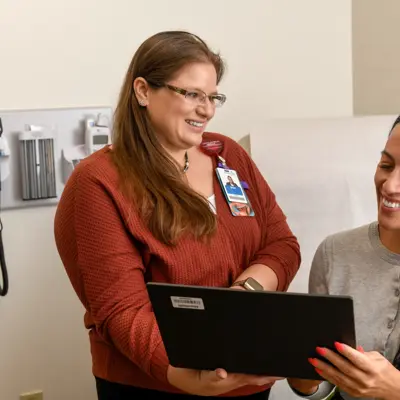 Two women in a hospital room, one showing the other something on a tablet.