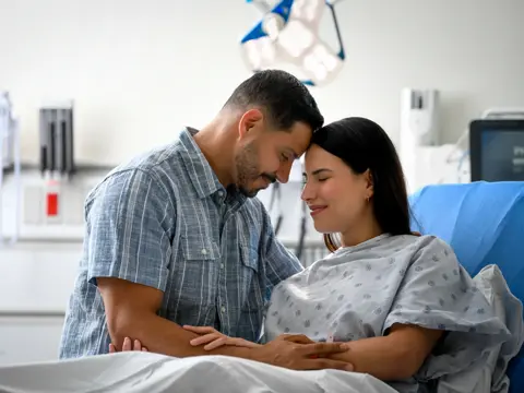 A man and woman in a hospital room, smiling and holding hands.