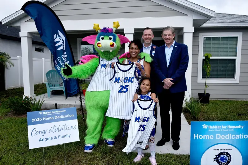 A family holding up Orlando magic gear in front of a house with AdventHealth Officials.