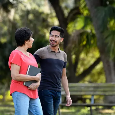 A smiling woman and man walking together in a park, she holds a book.
