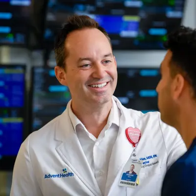 Two smiling nurses engaged in conversation in a hospital setting with medical monitoring equipment visible in the background