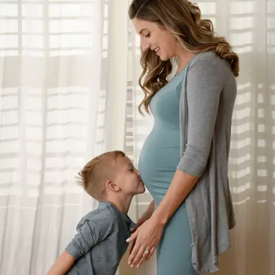 A pregnant woman and a young boy standing close together, smiling and looking at each other.