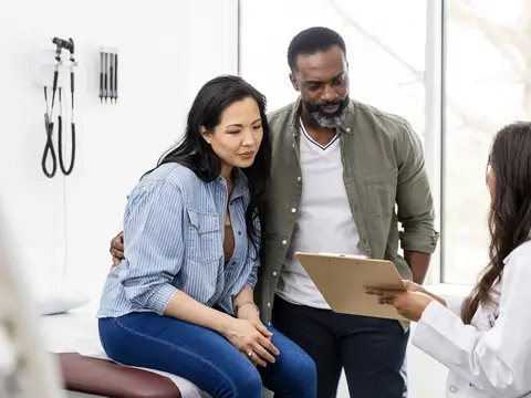 Two adults review a clipboard with a person in a white coat beside an exam table.