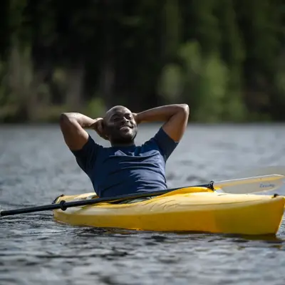 Man in a yellow kayak on a lake, smiling and relaxing with his arms behind his head.