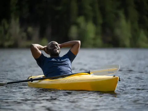 Man in a yellow kayak on a lake, smiling and relaxing with his arms behind his head.