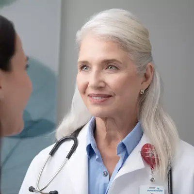 A smiling doctor with a stethoscope around her neck talks to a patient.