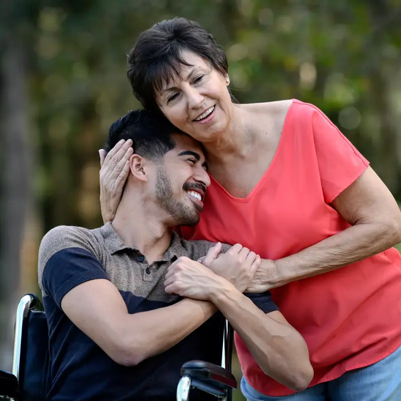 A smiling woman embraces a man in a wheelchair, both looking happy and content.