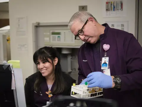 A smiling woman and a man in lab coats examining a test tube in a medical lab.