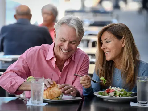 A smiling man and woman enjoy a meal together at an outdoor restaurant, showcasing a moment of shared joy and connection.