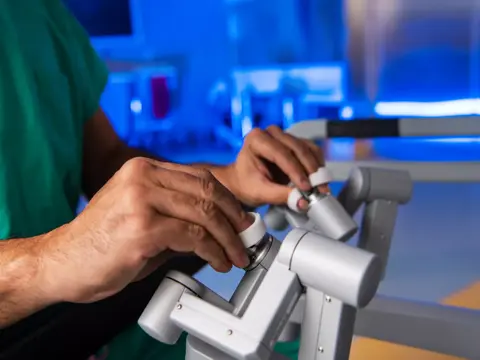 A surgeon in green scrubs adjusts a robotic surgical device in an operating room.