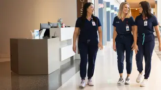 Three Nurses Smiling and Walking Together Calmly Down a Hospital Hallway.