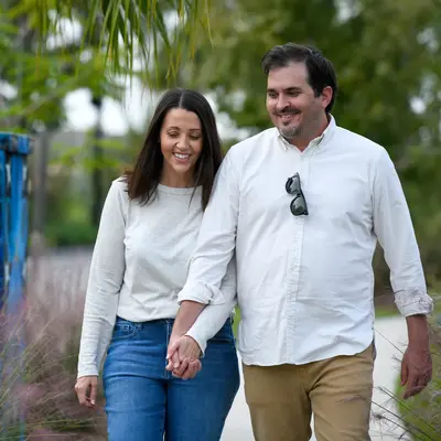 A smiling couple walking hand in hand in a park with colorful art and greenery.