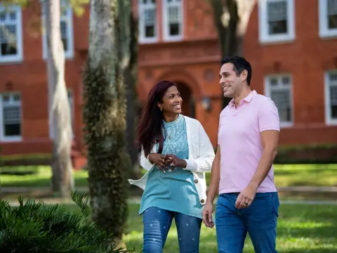 A smiling couple walking hand in hand in front of a brick building.