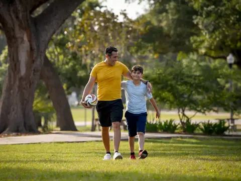 Father and son walking in park, holding hands and soccer ball.