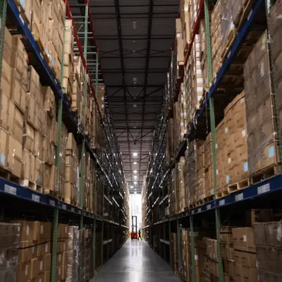 A long aisle in a warehouse filled with shelves of stacked cardboard boxes.
