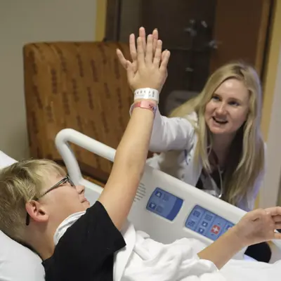 A young boy in a hospital bed high-fiving a nurse, both smiling.