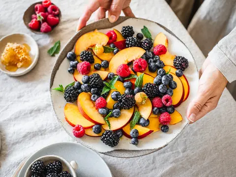 A plate of peaches and berries, held above a table.