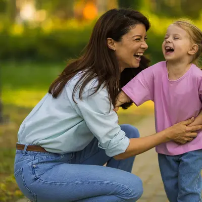 A woman playing with her young daughter outdoors.