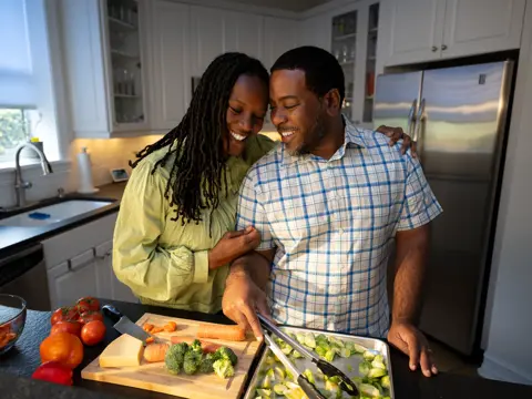 A smiling couple in a kitchen preparing food together, showcasing a warm and engaging atmosphere.
