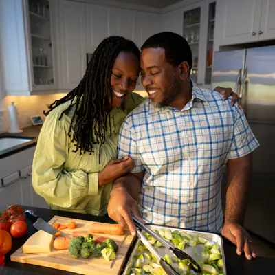 A smiling couple in a kitchen preparing food together, showcasing a warm and engaging atmosphere.