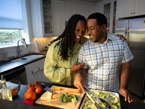 A smiling couple in a kitchen preparing food together, showcasing a warm and engaging atmosphere.