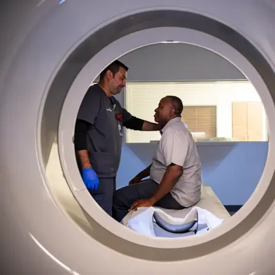 A healthcare professional assists a patient inside a large, circular medical imaging machine.