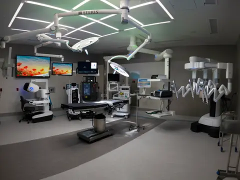 Modern surgical room with advanced medical equipment, monitors, and robotic systems.