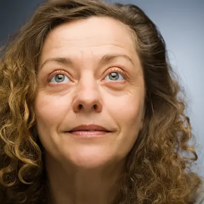Woman with curly brown hair looks slightly upward against a gradient blue-gray background.