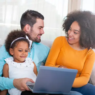 Family of three sitting on a sofa looking at a laptop