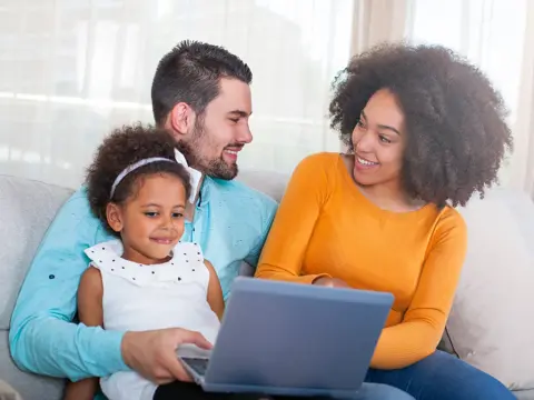Family of three sitting on a sofa looking at a laptop