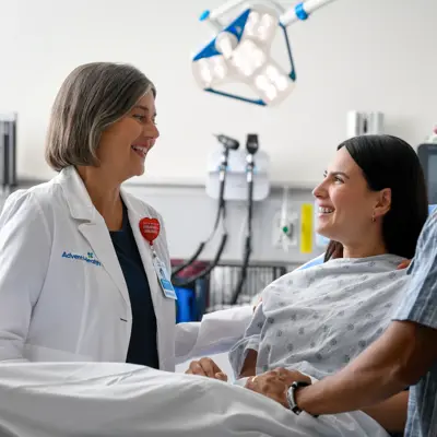 A smiling doctor and a man comfort a smiling woman in a hospital bed.