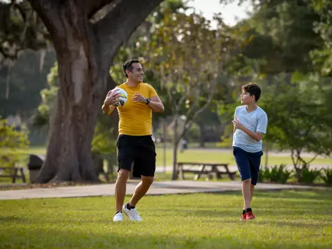 A man and a boy play with a soccer ball in a park, showcasing active family bonding.
