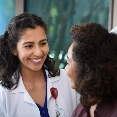 A smiling doctor in a white coat talks to a patient, conveying warmth and care.
