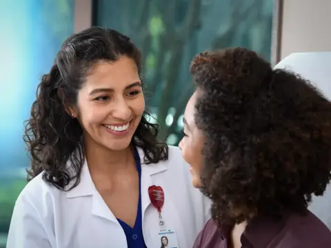 A smiling doctor in a white coat talks to a patient, conveying warmth and care.