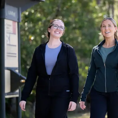 Two women walking together on a path, smiling and holding hands.